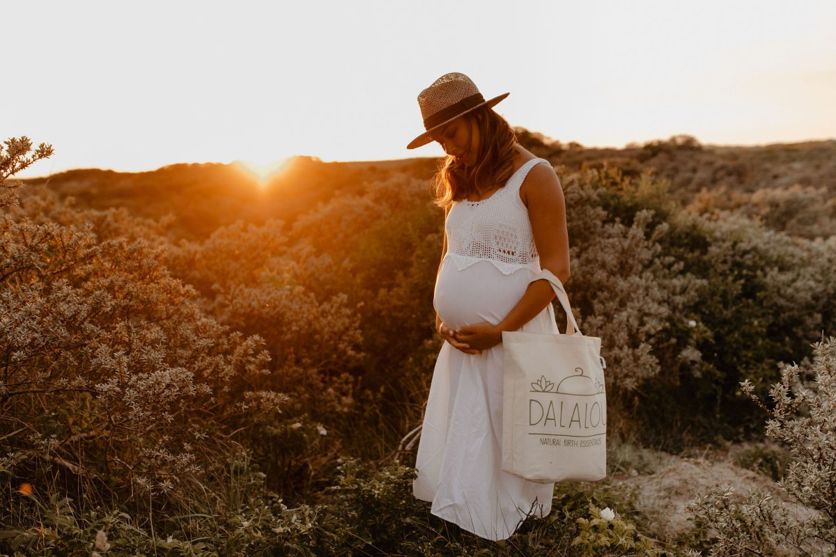 zwangere vrouw bekijkt buik buiten in natuur bij zonsondergang