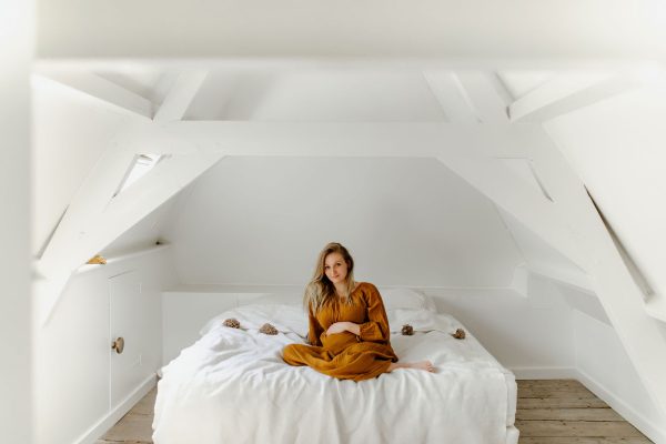 zwangere vrouw zit op bed en lacht naar camera