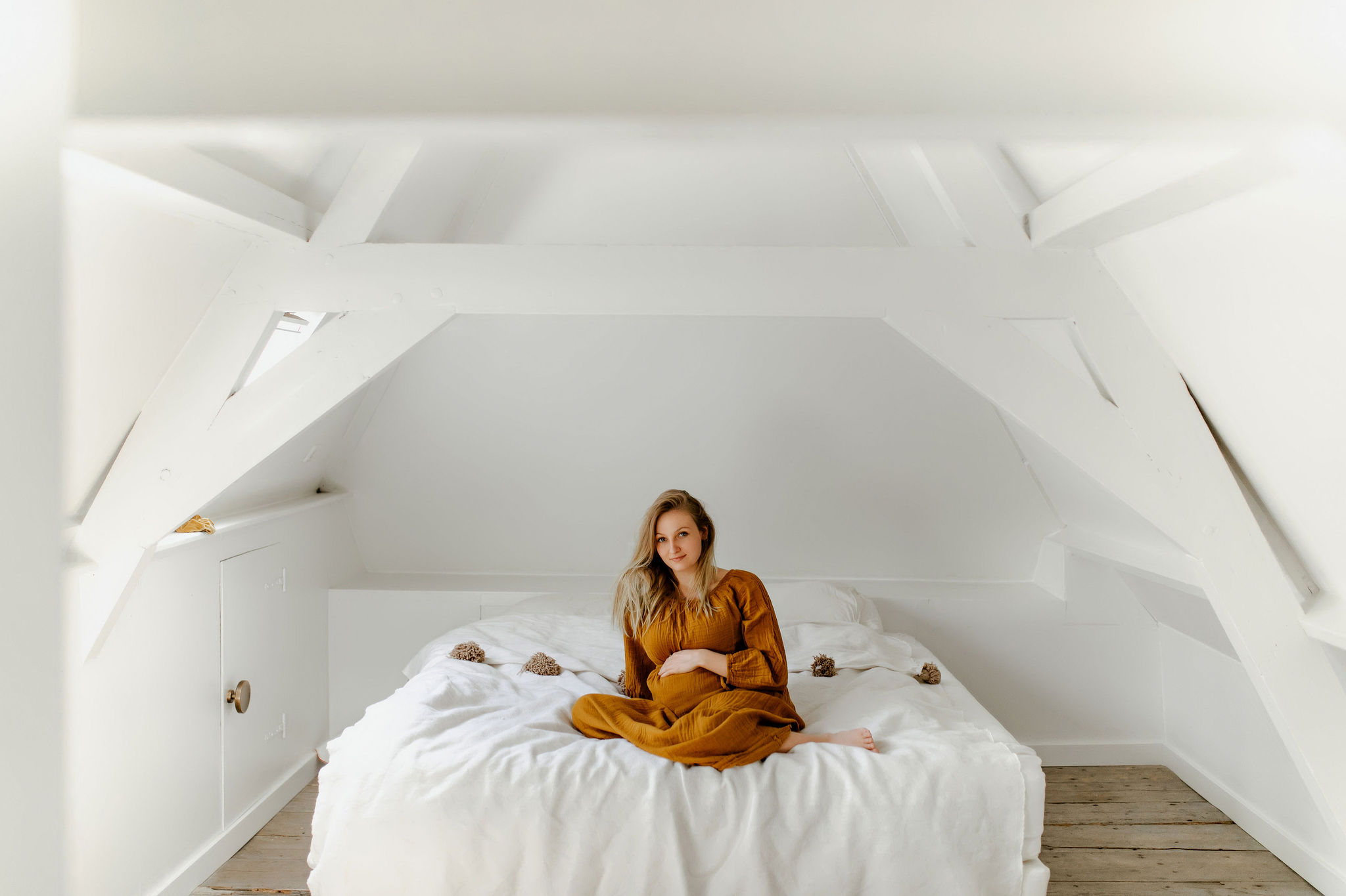 zwangere vrouw zit op bed en lacht naar camera